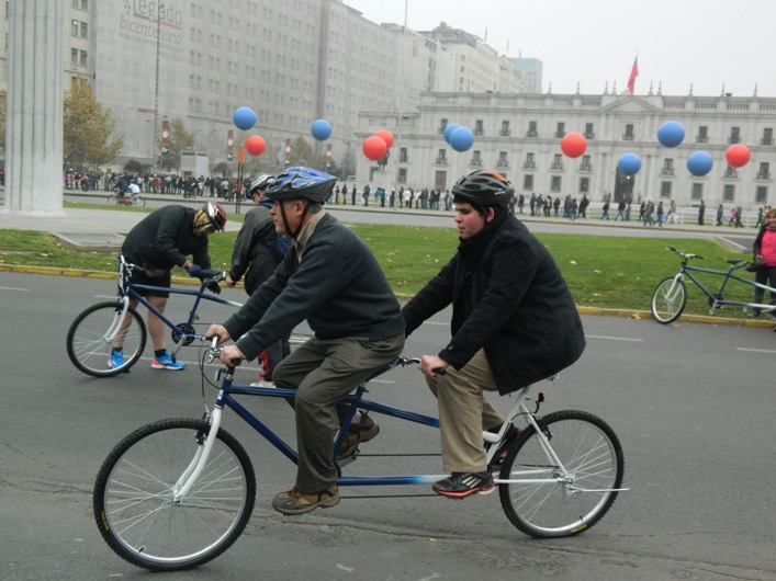 Personas transitan en una bicicleta Tándem por la Alameda frente a La Moneda.