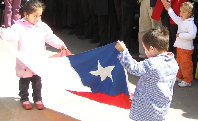 Una niña y un niños sostienen una bandera chilena