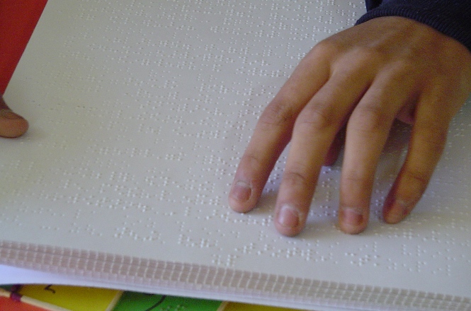 La mano de un joven con discapacidad visual  sobre un texto en sistema Braille