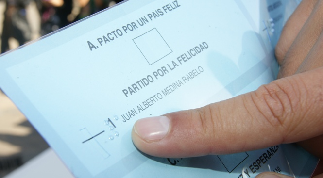 Plantilla para el voto y sobre ella un dedo indicando el sistema Braille