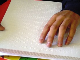 Se muestra unos dedos sobre un texto en sistema Braille