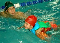 En la fotografía aparece un niño nadando en la piscina junto a un terapeuta.