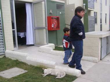 Una persona con una amputación en su brazo y un niño van saliendo de una casa que cuenta con rampa de acceso. 