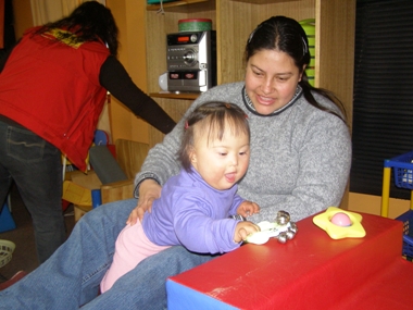 Una mujer tiene en sus brazos a su hija que presenta síndrome de Down, ambas están en una sala de rehabilitación.