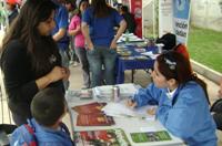 La profesional Jocelyn Franco en stand institucional entregando información a una mujer y su hijo