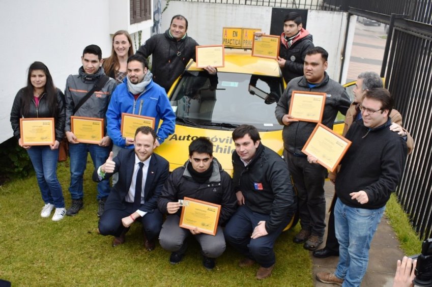 Personas sordas muestran sus diplomas del curso de conducción junto a un auto de práctica.