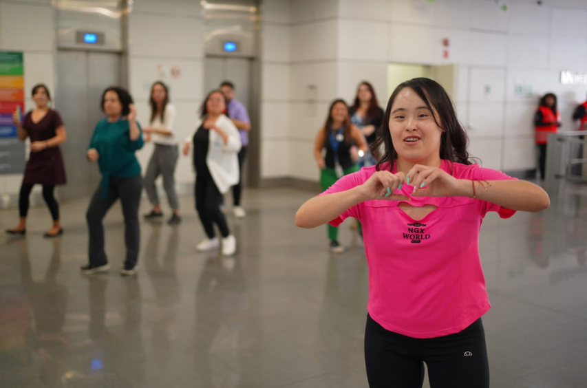 Foto grupal en la que una joven con Síndrome de Down guía una rutina de zumba. 